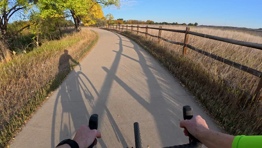 First person POV from riding a touring bike on a paved trail along the Poudre River in northern Colorado near Windsor, fall scenery with cyclist shadow