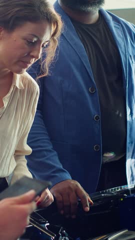 Vertical video Salesman showing components under car hood for customers, hoping to close deal. Showroom agent trying to persuade clients to make purchase by presenting parts used to make vehicle