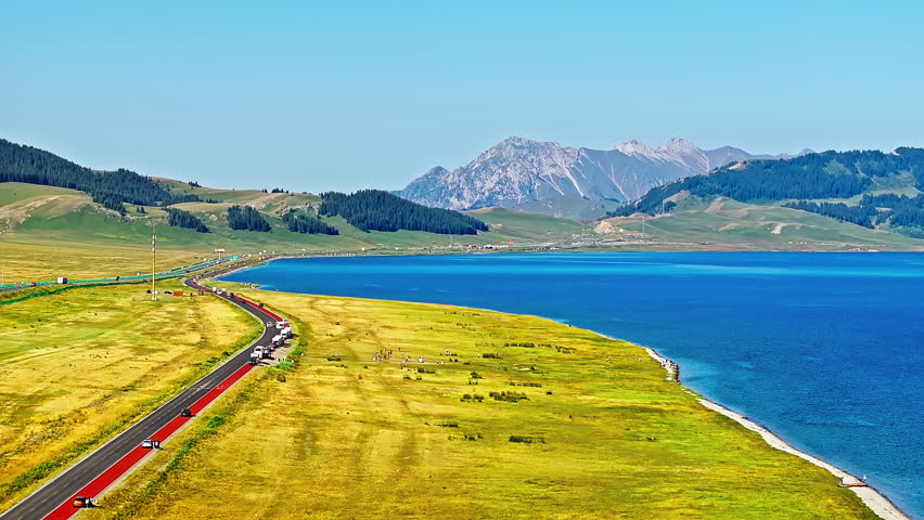 Aerial video of the beautiful Sayram Lake natural landscape in Xinjiang. Yellow grass and blue lake with mountain scenery under the blue sky. Famous travel destination in China.