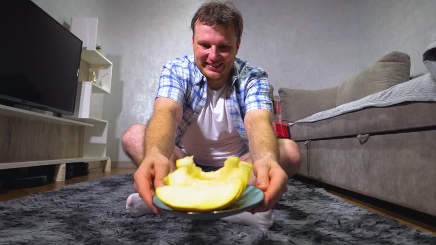 A young handsome man eats a ripe melon at home. Fruit Melon in a plate. Slow motion