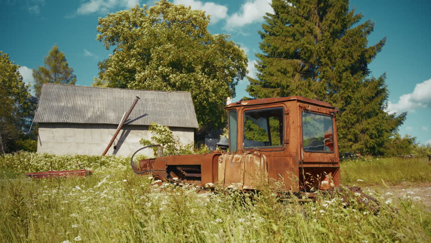 Old rusty tractor remains in an overgrown abandoned farm land during daytime in summer