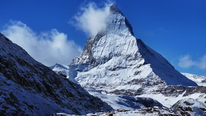 The Matterhorn famous mountain peak rocky cliffs Riffelsee Lake Zermatt Swiss Alps aerial drone wind fog first fresh snow fall autumn winter blue skies morning Gornergrat railway Switzerland upward