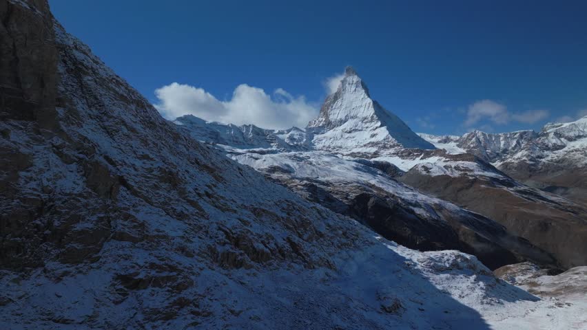Matterhorn famous mountain peak rocky cliffs Riffelsee Lake Zermatt Swiss Alps aerial drone first fresh snow fall autumn winter blue skies morning Gornergrat railway Switzerland upward slowly motion