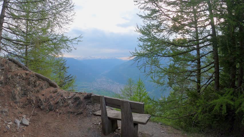 POV Wooden Bench At Viewpoint Overlooking The Mountain Range And Village In Daytime. - wide shot