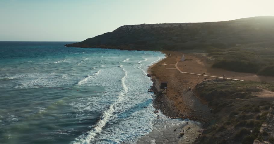 Aerial view of Ramla beach on the island of Gozo, Malta. Beautiful landscape of Mediterranean nature at sunset. Waves crash on sand and rocks, travel and tourism in Europe. High quality 4k footage