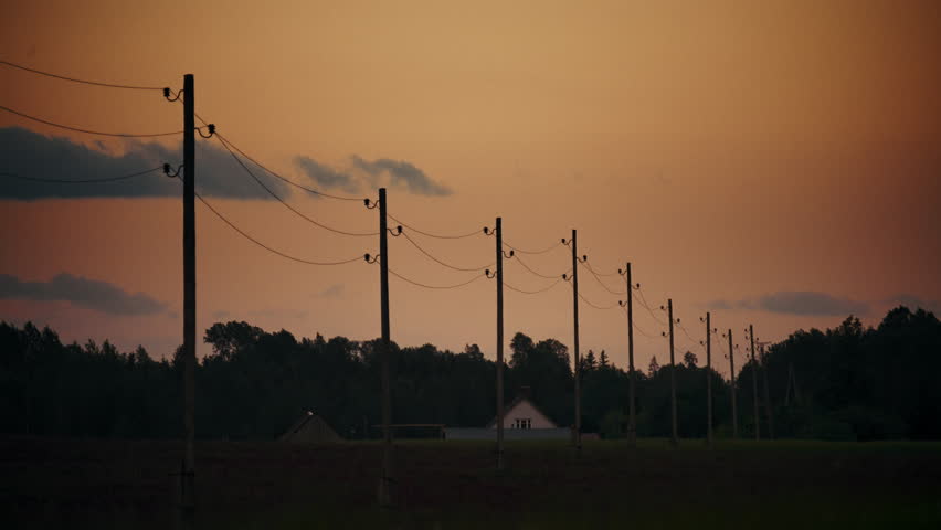 Electricity lines stretching across farm land in the countryside during sunset with clouds in the sky