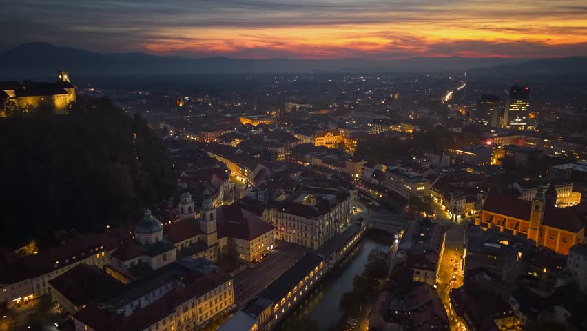 Epic sunset over Ljubljana Old Town reveals vibrant city lights and historical architecture illuminating the skyline. Aerial shot of evening Ljubljana, Slovenia. 4K HDR