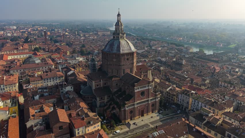 Breathtaking aerial view of the historic cathedral in Pavia, Italy, surrounded by charming rooftops and the serene river. Flying around Duomo di Pavia in Pavia old town at sunrise 