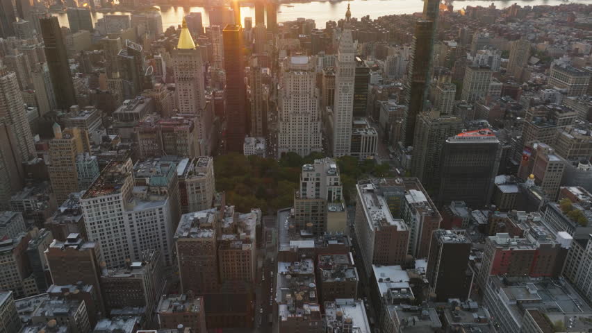 Aerial views showcase the sun illuminating Madison Square Park and surrounding buildings in New York City during a stunning sunset, highlighting the vibrant urban landscape