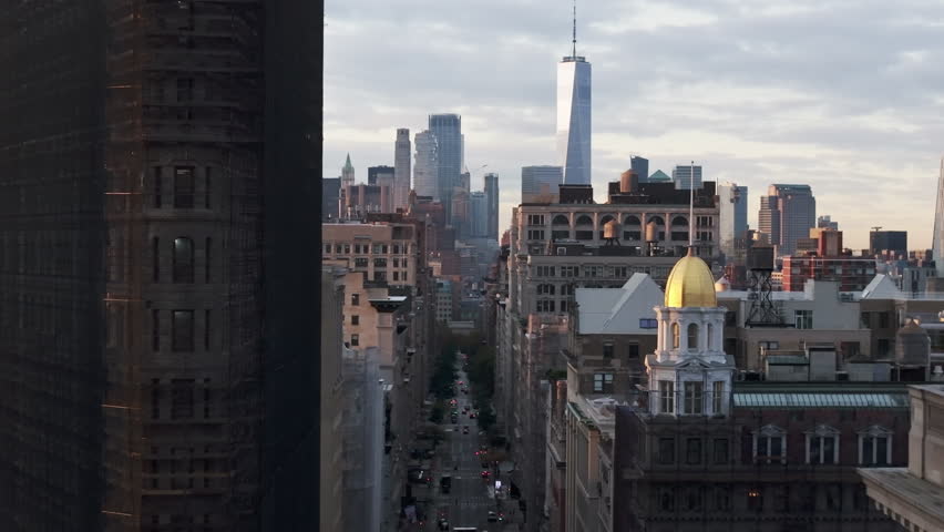 Camera pans over the Tribeca neighborhood in New York City. Residential and commercial buildings line the street with One World Trade Center in the background