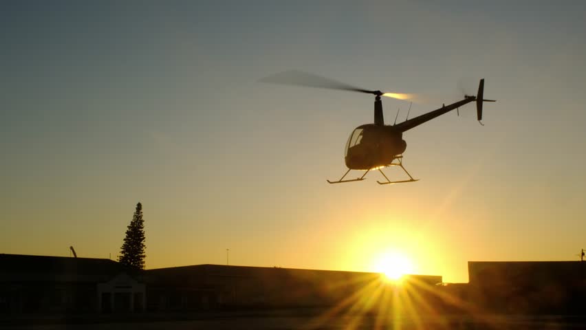Silhouette of a helicopter flying from above and descending for landing at the airport. Beautiful evening shot of an aircraft flies in front of the sun. Scenic cinematic slow motion footage