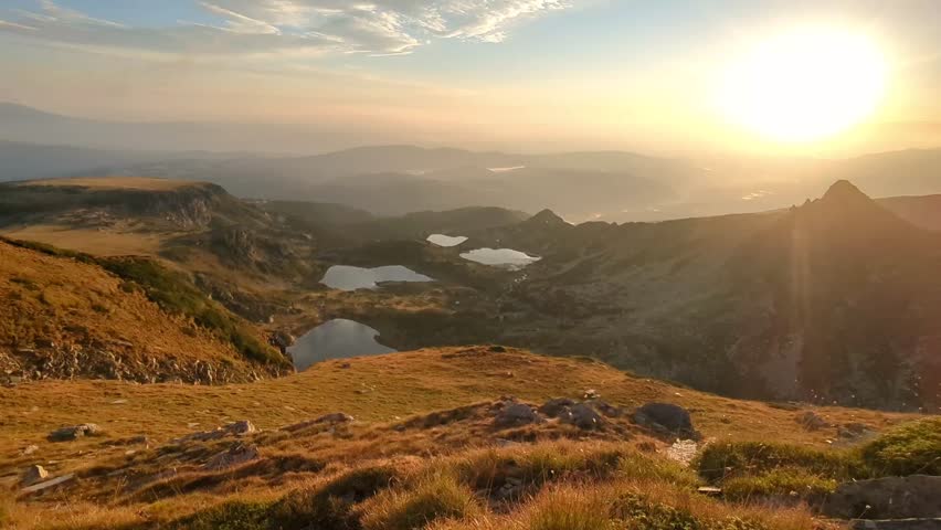 The Seven Rila Lakes in Bulgaria at dawn present a breathtaking view from the mountaintop, as early morning light reflects off the clear waters of the lakes surrounded by the rugged alpine terrain.