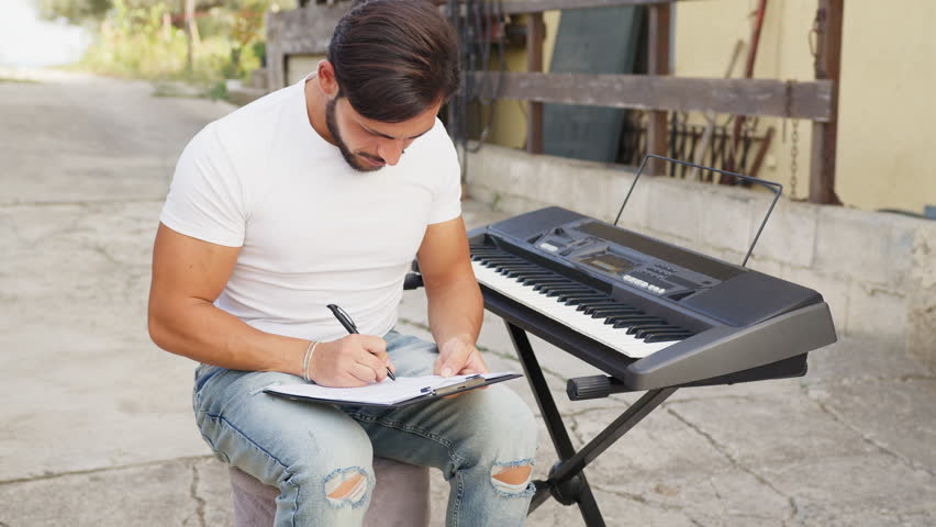 Man Is Composing A Music Writing On The Sheet Music And Rehearsing On Keyboard