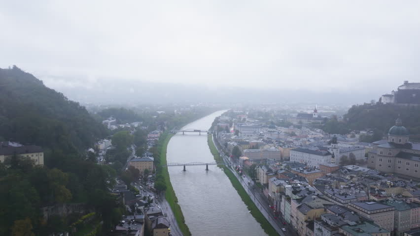 Aerial views of Salzburg, Austria, reveal the cityscape with the Salzach River, Hohensalzburg Fortress, and charming architecture under a cloudy sky