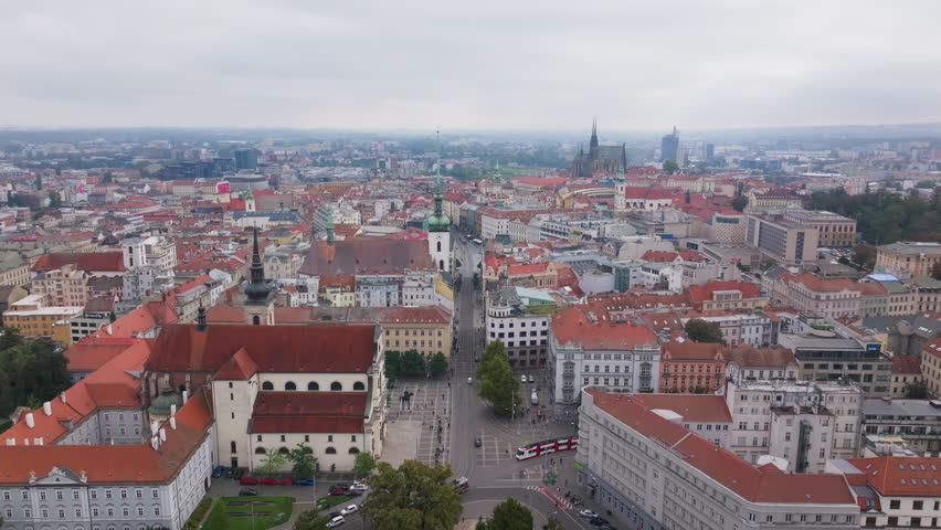 Slow pan over the city of Brno, Czech Republic. Red rooftops stretch out under a cloudy sky, with St Thomas