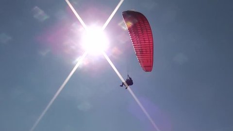 Parachute sliding with two people waving hands, passing the sun