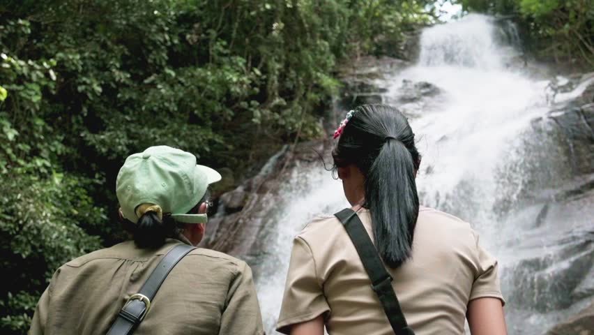 Mother and daughter hiking to admire the beautiful waterfall in tropical rainforest. Adventure and Outdoor pursuit. Ton Sung Waterfall, Phang Nga Province, Thailand.