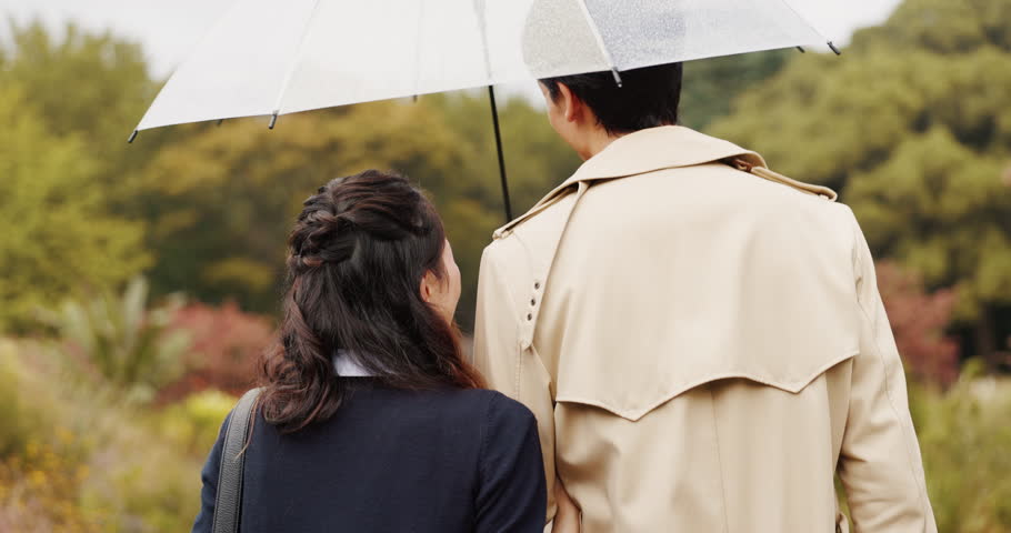 Park, umbrella and back of Asian couple walking for commute, journey and travel outdoors. Dating, autumn and man and woman in conversation, bonding and talking with protection for rainfall in Japan