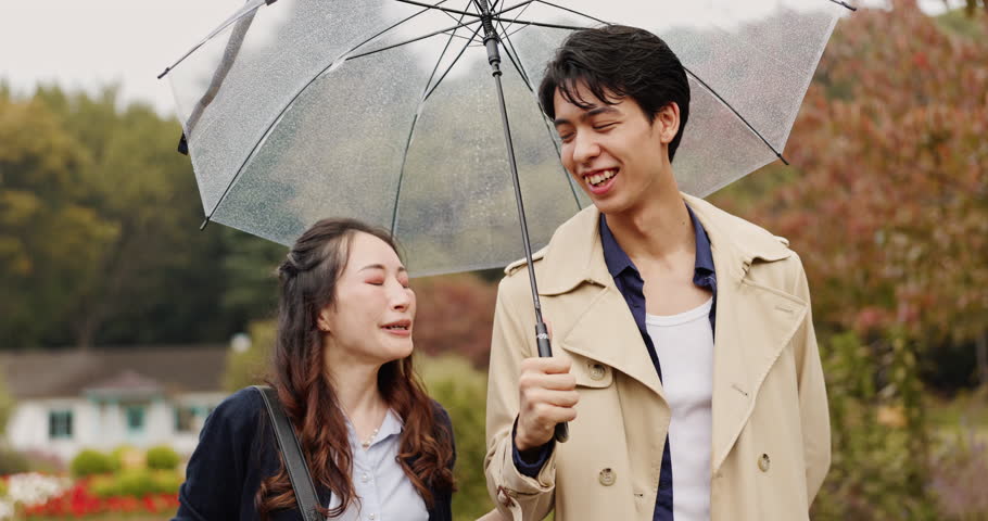 Walking, umbrella and Asian couple in park with rain for commute, journey and travel outdoors. Nature, autumn and Japanese man and woman in conversation with protection for drops, splash and water
