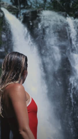 Vertical portrait: sexy sport girl stands in a waterfall Sekumpul. Female is on vacation. Beautiful face of woman. Tropical rainforest in jungle with rain in Bali. Great wild nature, Indonesia