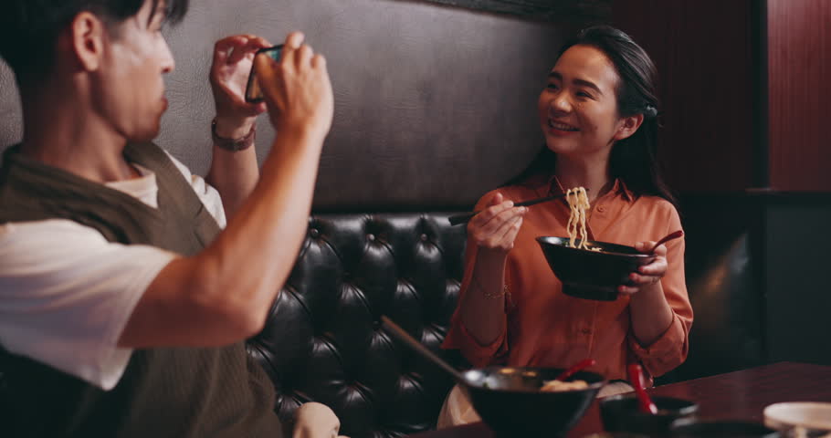 Asian couple, eating and camera with vlog for live recording, meal or ramen at restaurant. Japanese, man and happy woman with noodles for online streaming, dish or tasting cuisine or meal in Japan