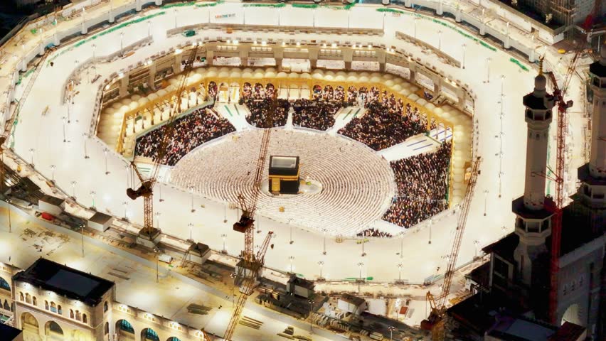 Illuminated aerial view of the Kaaba at night, surrounded by large crowds of pilgrims and bright lights, highlighting the spiritual atmosphere of the Grand Mosque in Mecca