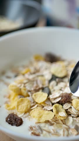 Spoon takes yogurt mixed with granola and cereal in a bowl in the process of eating food. Breakfast natural muesli mixed with cream and using a spoon. Vegetarian food and healthy diet. vertical