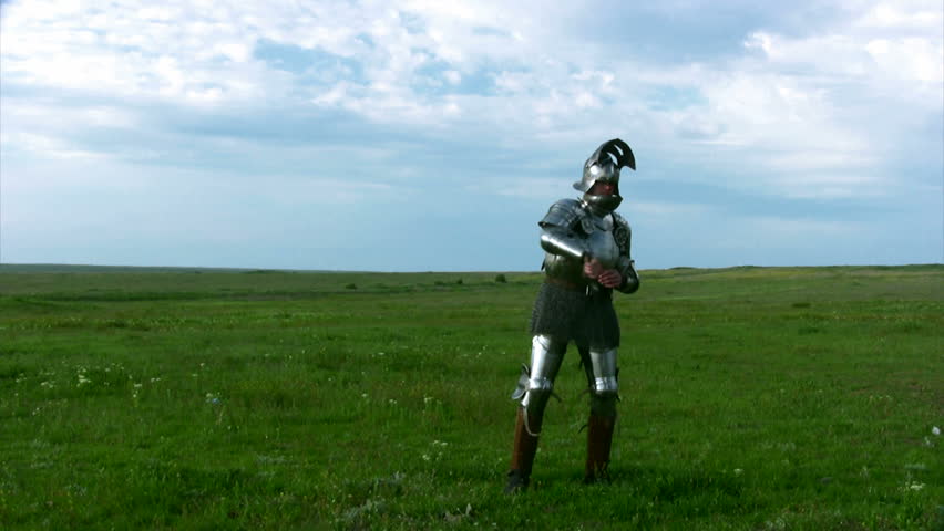 Medieval knight in armor, and with an open visor exercise with a sword against the backdrop of steppe grass and blue sky