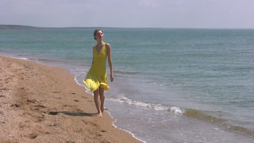 Slim pretty girl with curler in the yellow dress is on the edge of the water