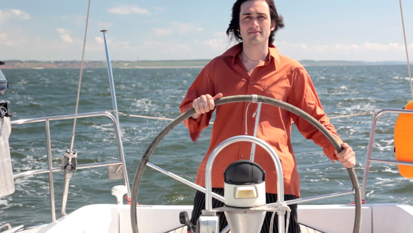 A young man in a red shirt standing at the controls of cruising yachts. In the