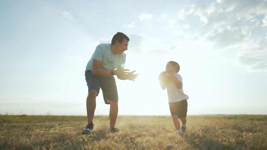 family playing ball on grass. Father son enjoying sunset together. Child holding ball father encouraging. Family bonding outdoors having fun. Sunset glow family playing ball. moment grass family time.