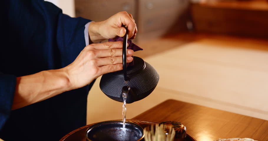 Person, tea ceremony and hands with teapot, matcha for Japanese tradition and culture, wellness and drink. Herb, ceramic kettle and cup for traditional detox, health and herbal custom at table
