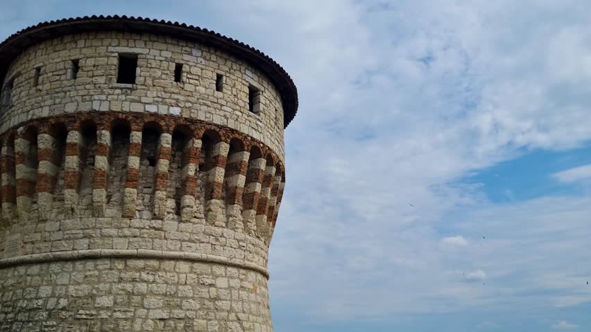 Swallows flying in front of main tower of the fortress of Brescia in Italy on a partly cloudy day
