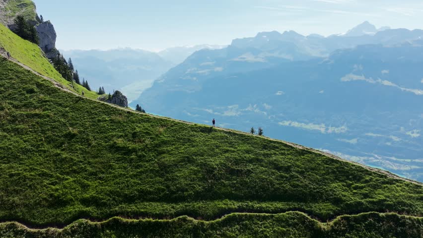 Hiker explores green mountain ridge with expansive lake views in the Swiss Alps