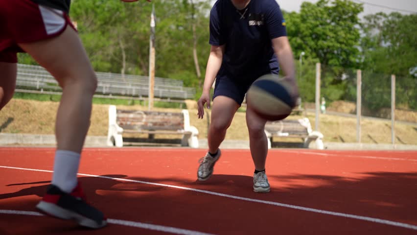 Close-up shot of two girls basketball players in sneakers and a blue sports uniform compete with each other with mastery of the ball while playing basketball on a summer sports field