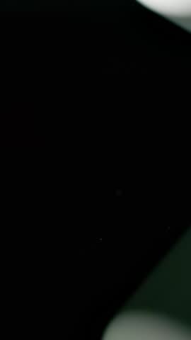 Pill bottle falls over and slips pills onto a black surface in slow motion. Vertical Video.
