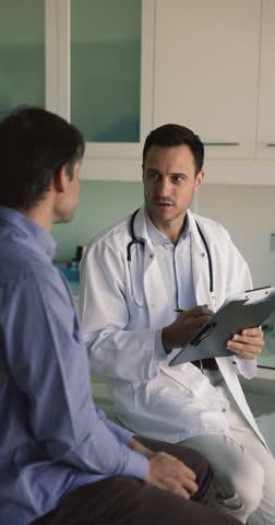 Mature male doctor in white uniform and stethoscope on neck talk to man patient, discuss concerns, writes health complaints, filling medical form card. General check-up, healthcare, medical insurance