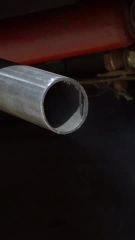 Vertical Slow motion closeup of thick white smoke billowing from a car exhaust pipe, releasing harmful carbon monoxide. The vehicle emits fumes on the road, air pollution in traffic