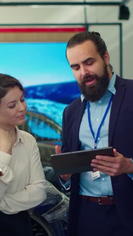 Vertical video Car dealership salesman showing product offerings on tablet to clients, making appropriate recommendations. Showroom agent presents financing options to customers on device, camera A