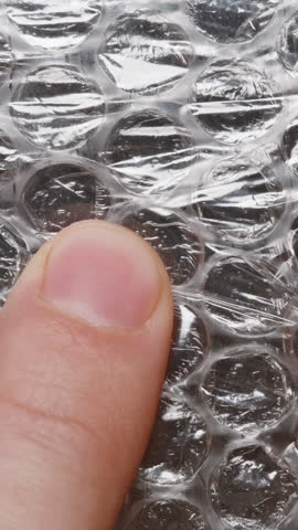 Vertical video. Close-up of male fingers pressing on bubble wrap, focusing on the tactile interaction as bubbles are popped, capturing the texture of the plastic surface for stress relief.