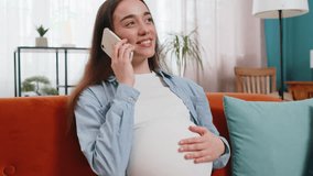 Smiling pregnant woman talking on smartphone sitting on sofa in living room at home. Happy Caucasian lady stroking belly holding cellphone in apartment. Maternity prenatal care and pregnancy concept. - Powered by Shutterstock - Get 15% off with code: PIKWIZARD15