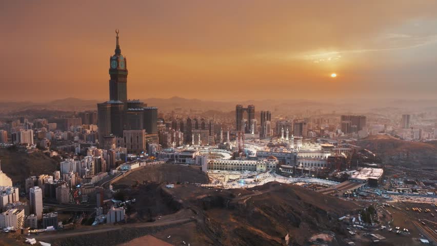 A breathtaking sunrise illuminating the Abraj Al-Bait Clock Tower and Grand Mosque in Mecca, surrounded by the sprawling city and mountains in a serene morning view