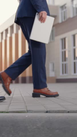 Business people walk along sidewalk, peoples walking feet. Office pedestrians walk along city street to work. City life of people. Man with briefcase in business suit walks next to business woman