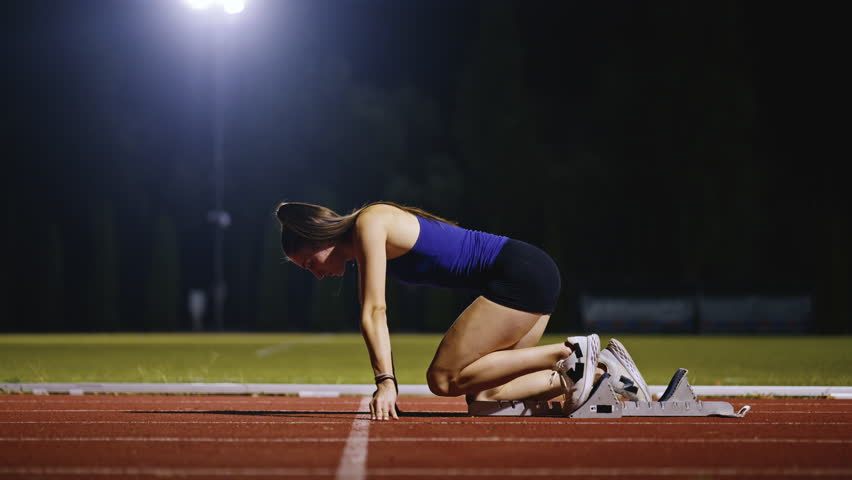 Female Runner on Athletics sprint race starting blocks on a dark background