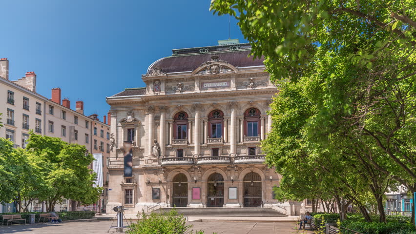 Timelapse hyperlapse of Theatre des Celestins in Lyon, France. A historic theatre on Place des Celestins with trees, benches and people relaxing under blue sky. Classic architecture and cultural charm