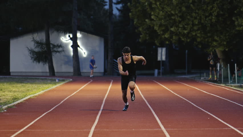 Vertical video of a young athlete running on an athletics track on a sunny morning along a lane of the track. Concept of sport and perseverance.