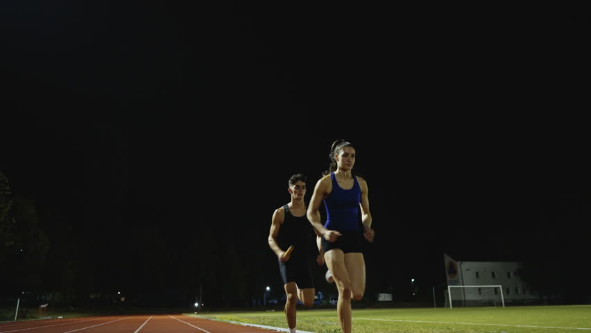 Athletes couple, male and female running a relay race and pass the baton on the athletics race track