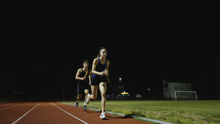 Athletes couple, male and female running a relay race and pass the baton on the athletics race track