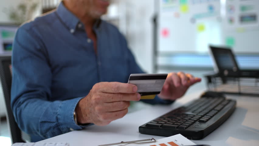 Manager holds a credit card while typing on a keyboard, processing an online payment in a business office setting - Powered by Shutterstock - Get 15% off with code: PIKWIZARD15