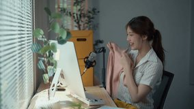Young asian woman livestreams from her home office, showcasing and discussing various clothing items with viewers - Powered by Shutterstock - Get 15% off with code: PIKWIZARD15